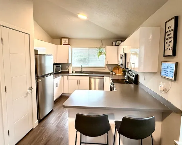 Kitchen featuring a peninsula, stainless steel appliances, white cabinets, a kitchen breakfast bar, and dark wood-style floors