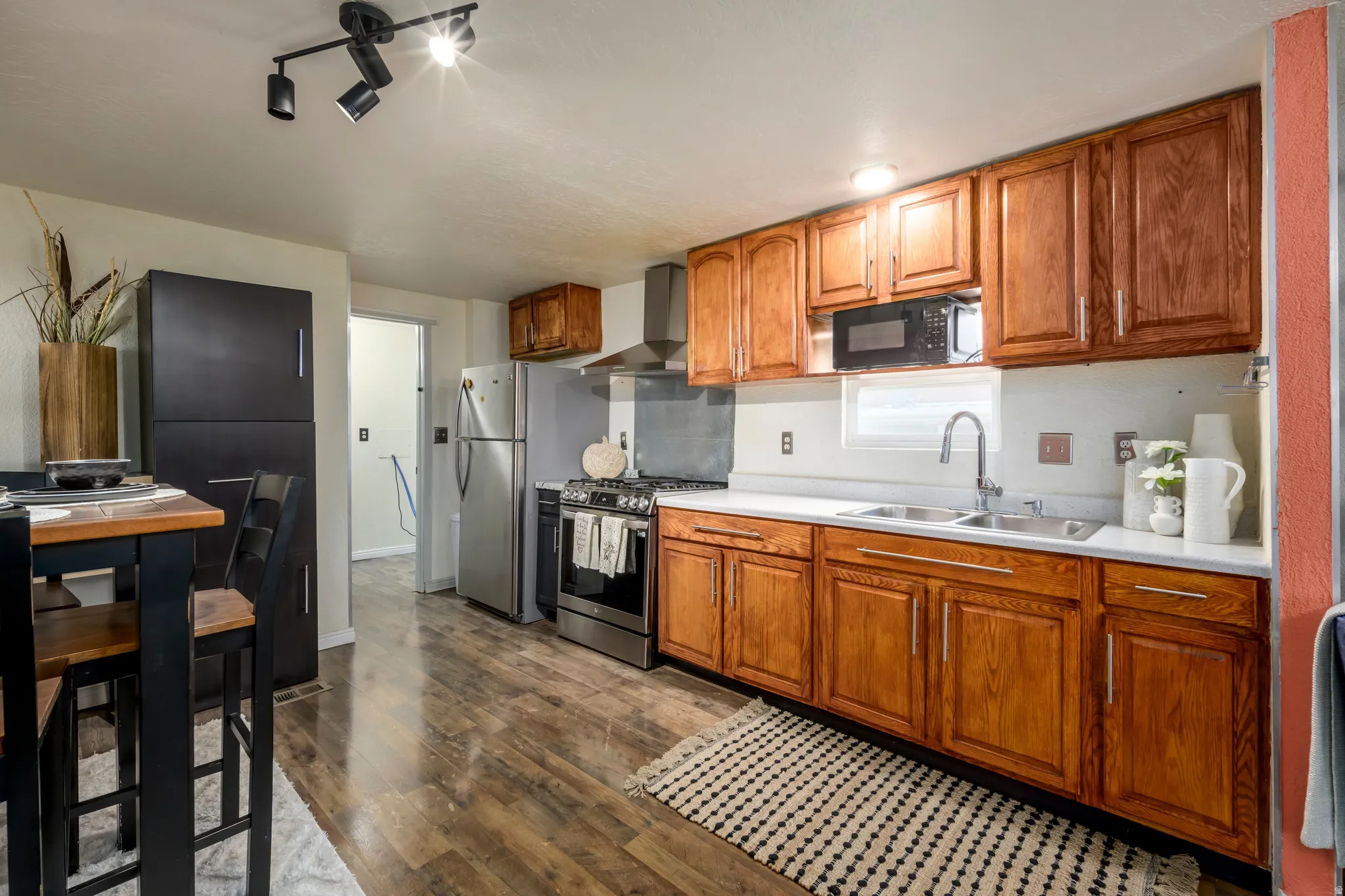 Kitchen featuring wood finish cabinetry, stainless steel appliances, light countertops, dark wood finished floors, and rail lighting
