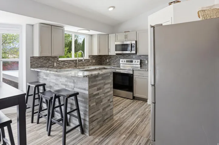 Kitchen featuring stainless steel appliances, a breakfast bar area, tasteful backsplash, light stone countertops, and vaulted ceiling