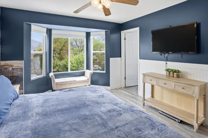 Bedroom with wood finished floors, a wainscoted wall, and a ceiling fan