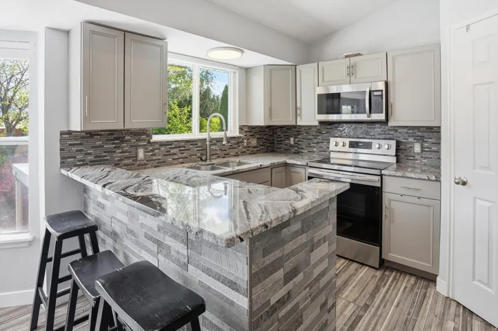 Kitchen with gray cabinets, stainless steel appliances, light stone countertops, lofted ceiling, and a peninsula