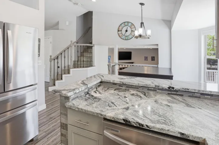 Kitchen featuring stainless steel appliances, light stone counters, hanging lights, and lofted ceiling