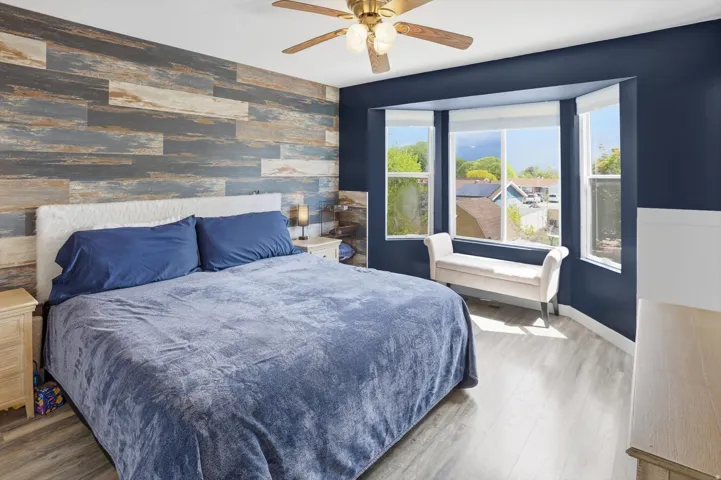 Bedroom featuring an accent wall, wallpapered walls, wood finished floors, and a ceiling fan