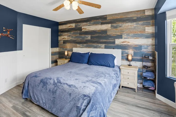 Bedroom with an accent wall, a closet, wood finished floors, a ceiling fan, and wooden walls