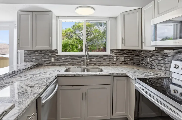 Kitchen with stainless steel appliances, light stone countertops, and gray cabinetry