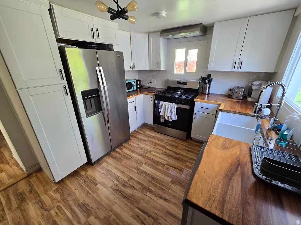 Kitchen featuring butcher block countertops, stainless steel appliances, white cabinetry, decorative backsplash, and dark wood finished floors