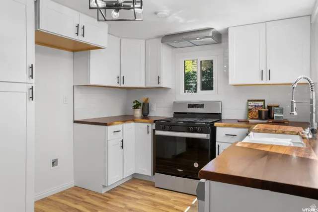 Kitchen with wood counters, gas stove, light wood-style flooring, white cabinetry, and range hood