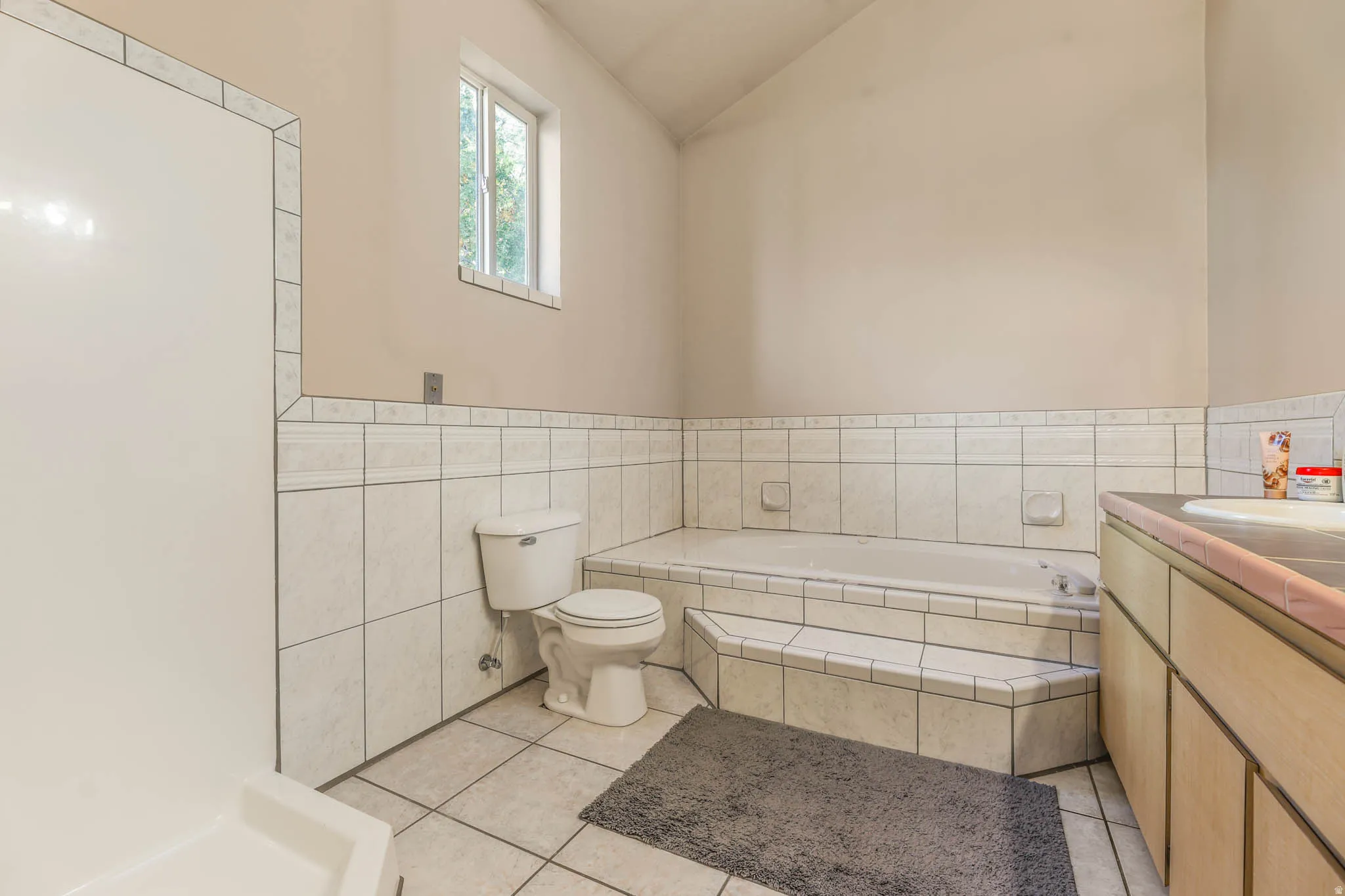 Full bath featuring vanity, a garden tub, light tile patterned floors, lofted ceiling, and tile walls