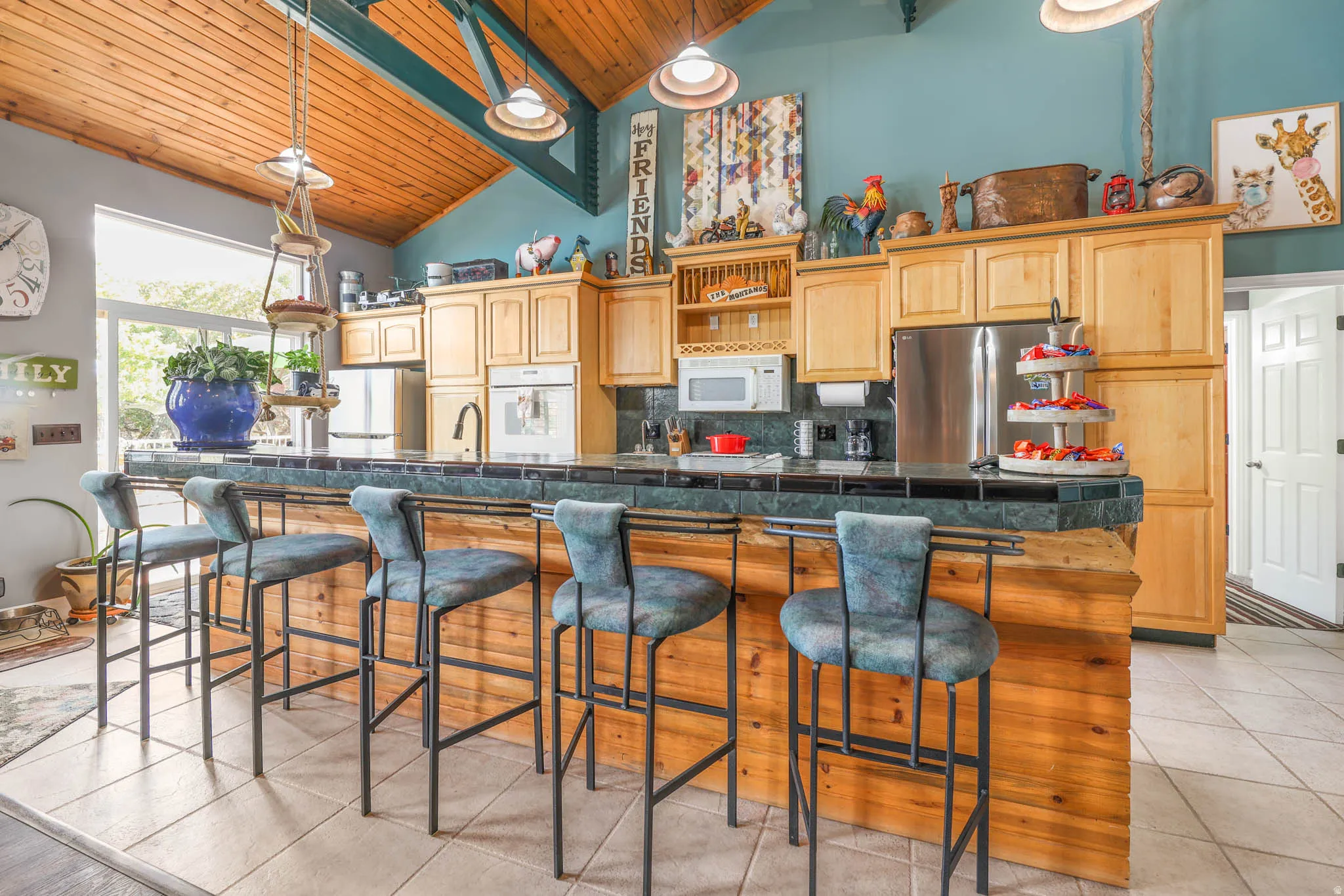 Kitchen featuring a kitchen breakfast bar, a large island, white appliances, light tile patterned floors, and a vaulted wooden ceiling