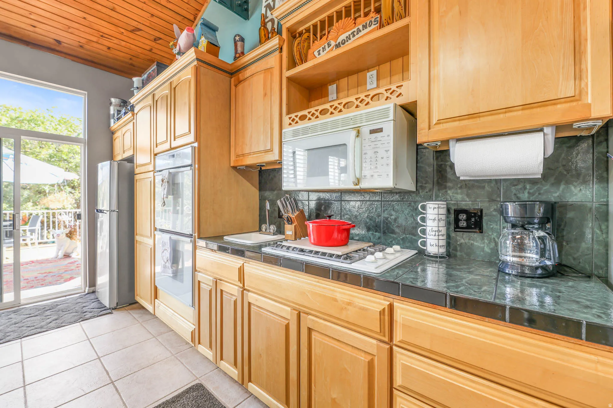 Kitchen with white appliances, tasteful backsplash, light tile patterned floors, wooden ceiling, and light wood finish cabinets