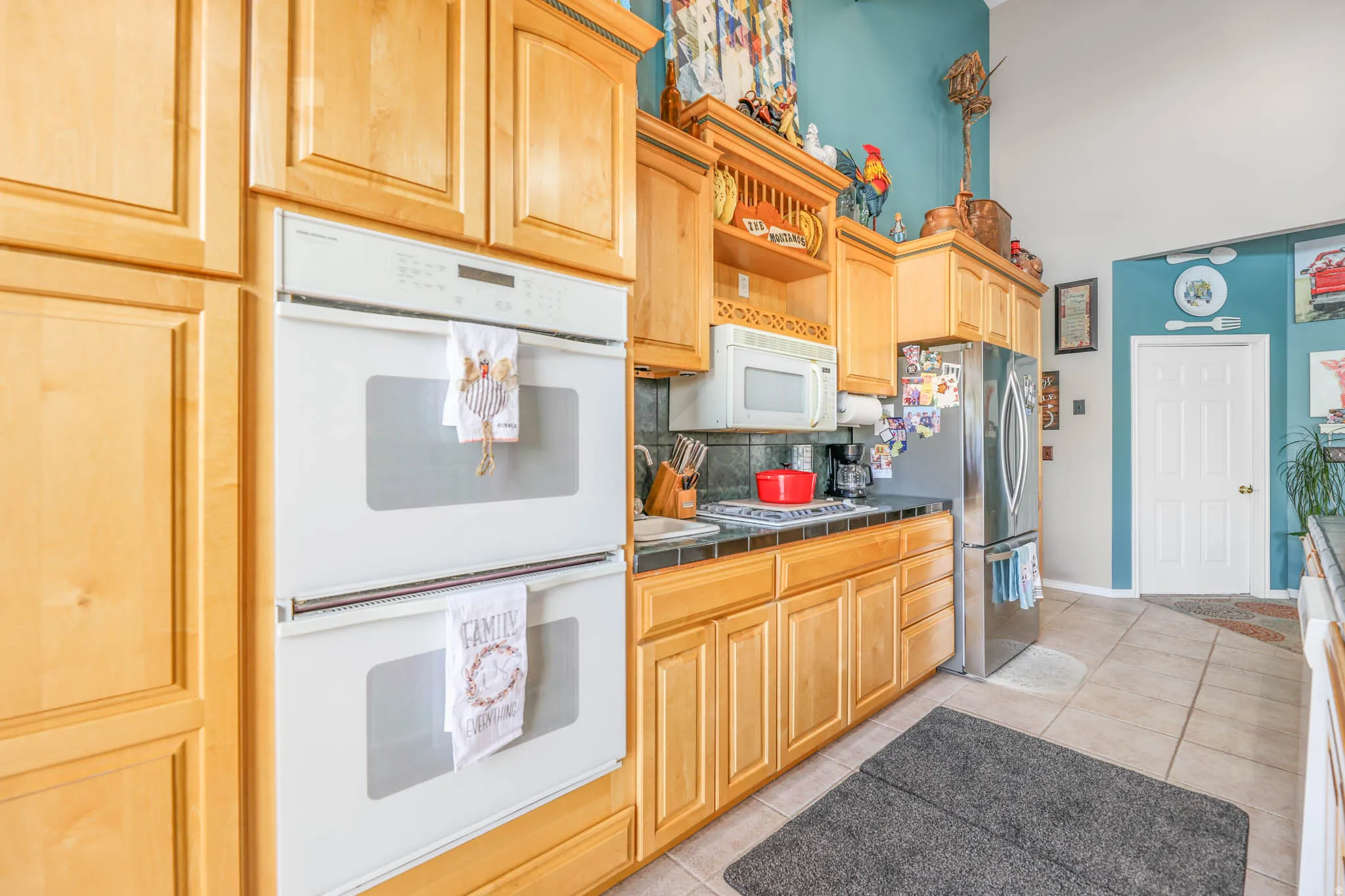 Kitchen with stainless steel appliances, light wood finish cabinets, backsplash, light tile patterned flooring, and tile countertops