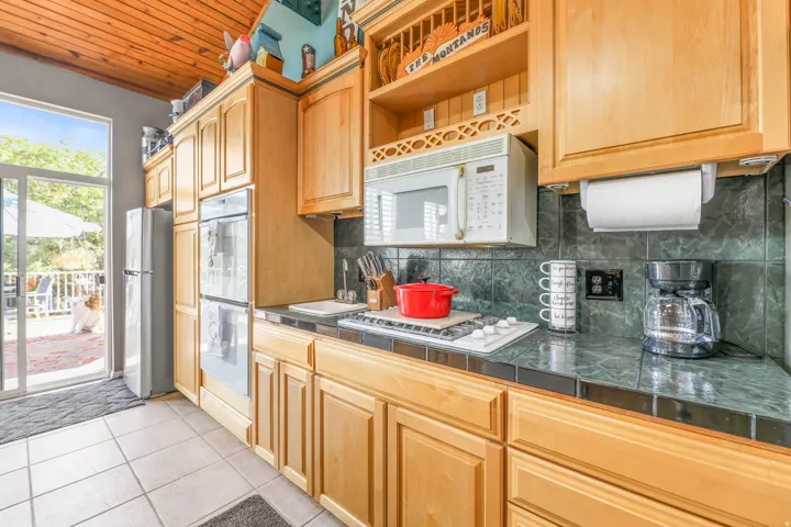 Kitchen with white appliances, tasteful backsplash, light tile patterned floors, wooden ceiling, and light wood finish cabinets