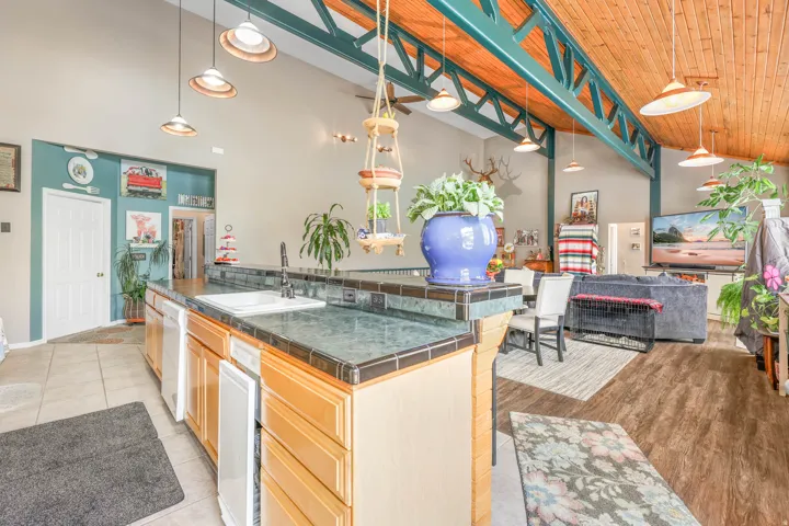 Kitchen with pendant lighting, a vaulted wooden ceiling, open floor plan, white dishwasher, and a kitchen breakfast bar