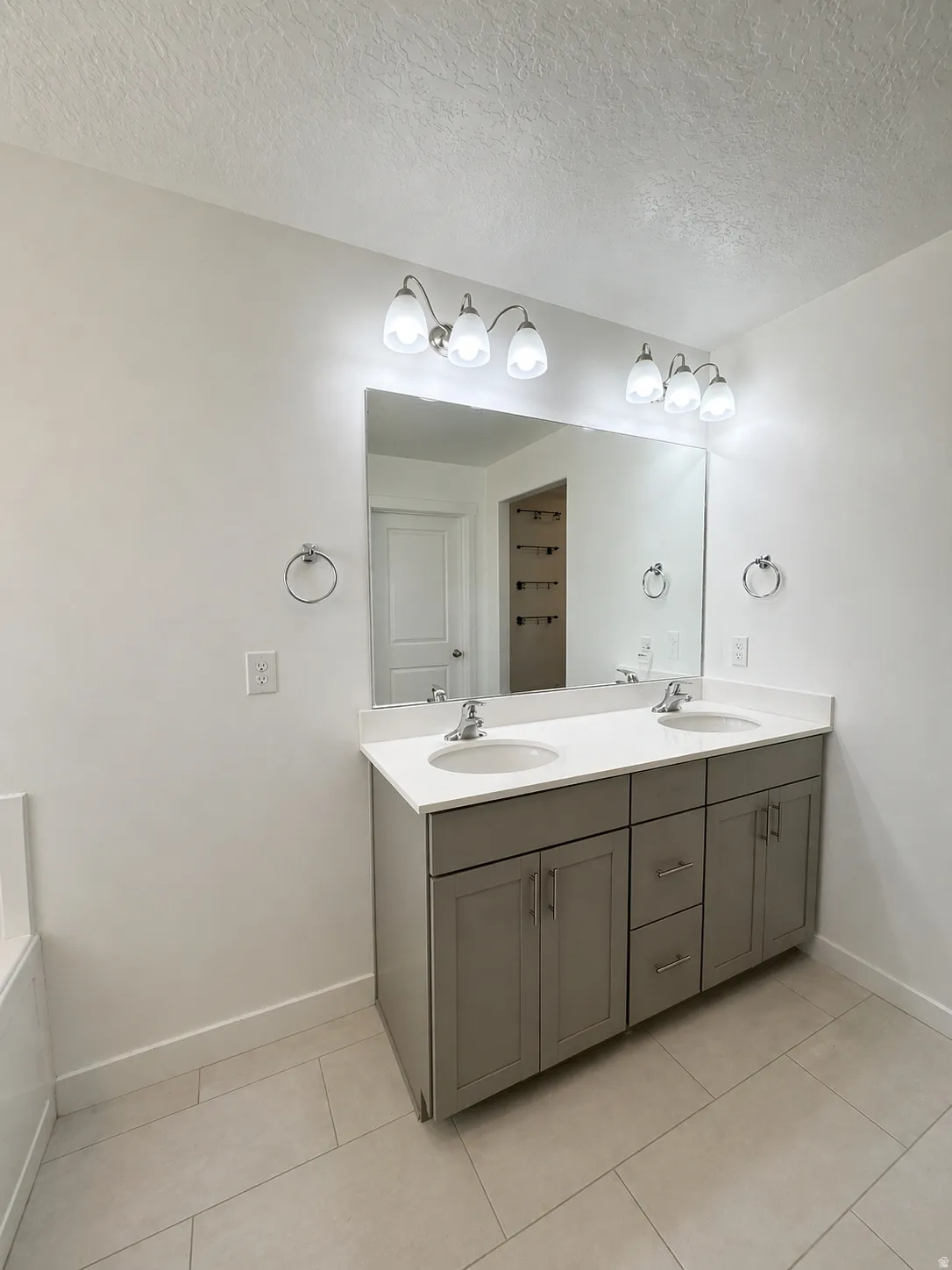 Bathroom featuring double vanity, a textured ceiling, and light tile patterned flooring