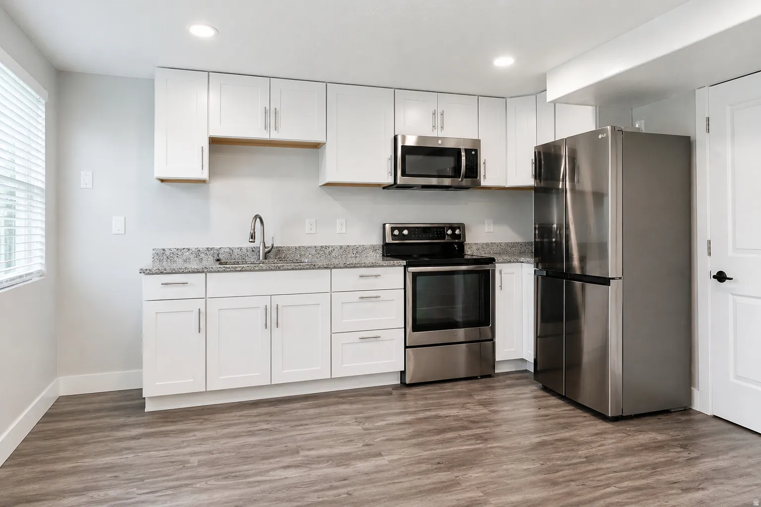 Kitchen with stainless steel appliances, light stone counters, white cabinetry, dark wood-style floors, and recessed lighting