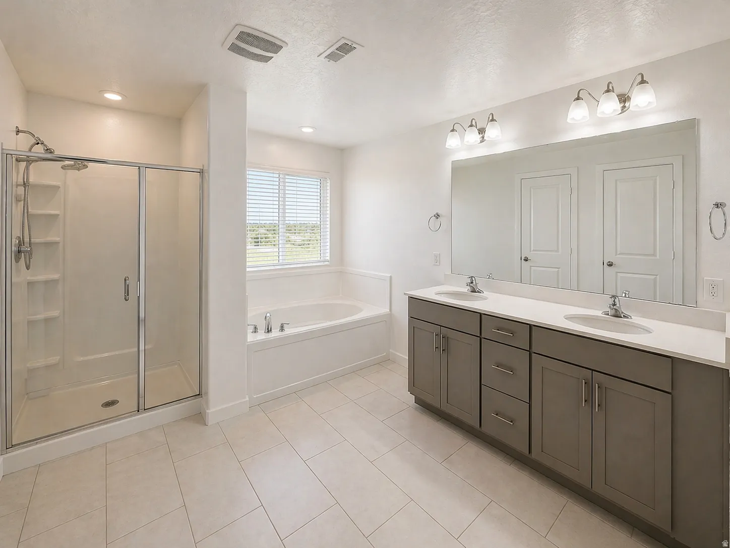 Full bath with double vanity, a bath, a stall shower, light tile patterned flooring, and a textured ceiling