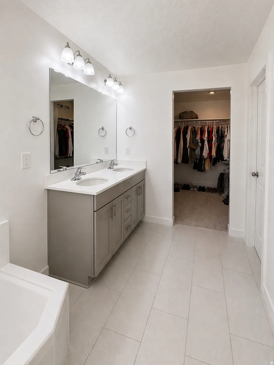 Bathroom featuring a spacious closet, double vanity, light tile patterned flooring, a textured ceiling, and a garden tub