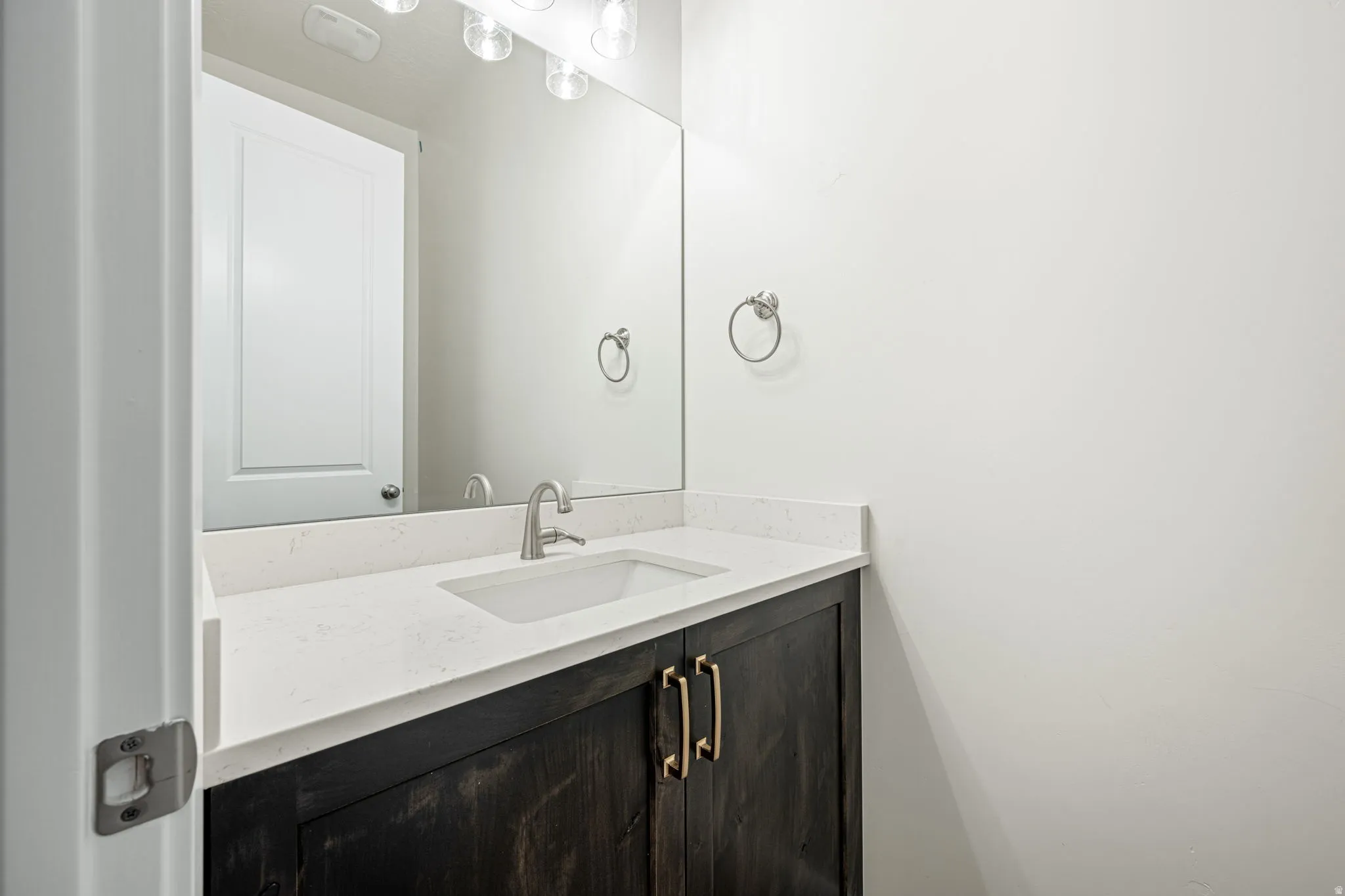 Vanity with dark wood-finish cabinetry, brushed nickel hardware, and a white countertop featuring an integrated rectangular sink
