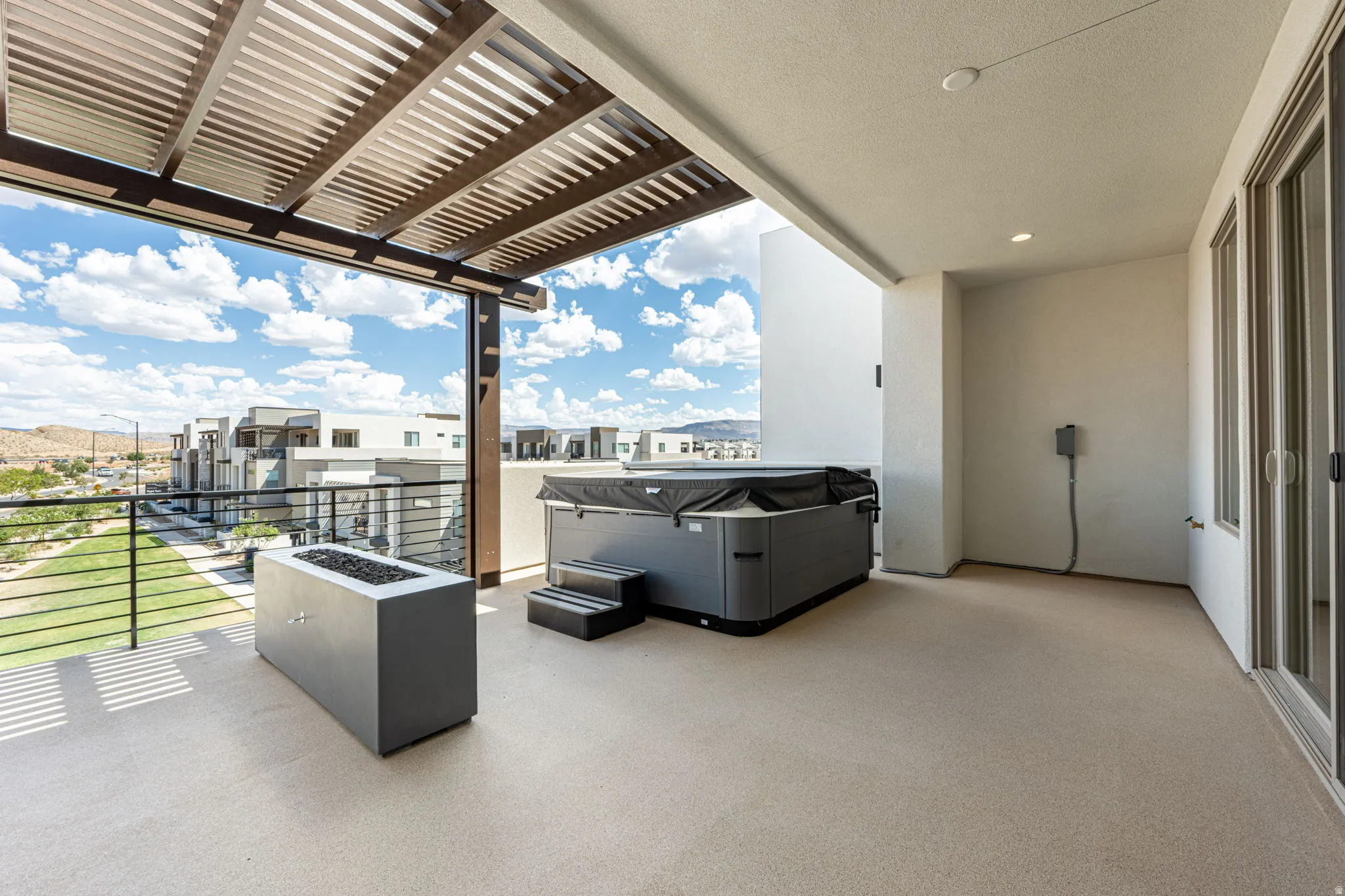 Spacious outdoor patio featuring a slatted pergola, integrated fire pit, and an outdoor spa with steps