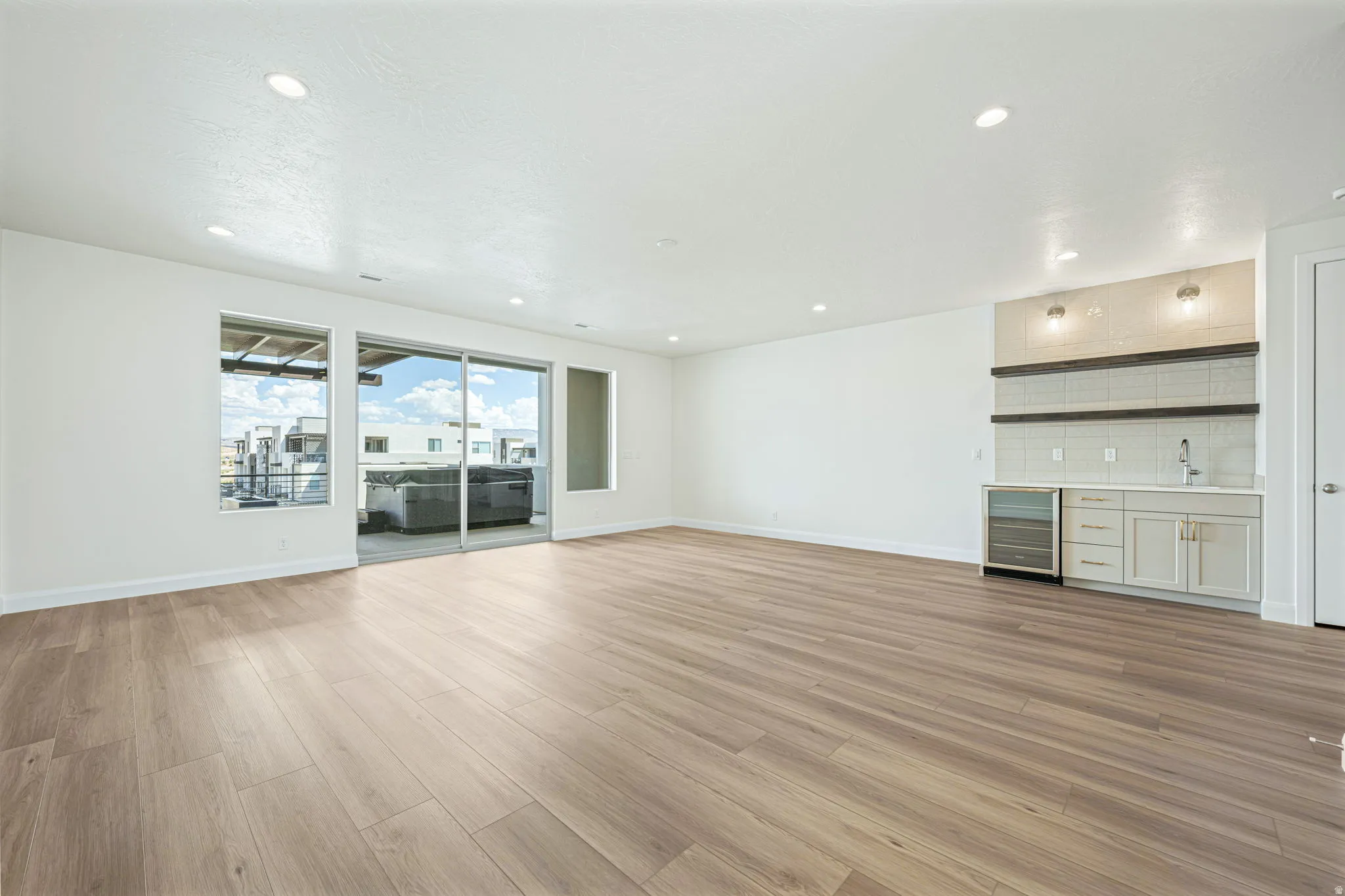 Spacious room featuring wood-finish flooring, recessed lighting, and a built-in wet bar with a beverage cooler