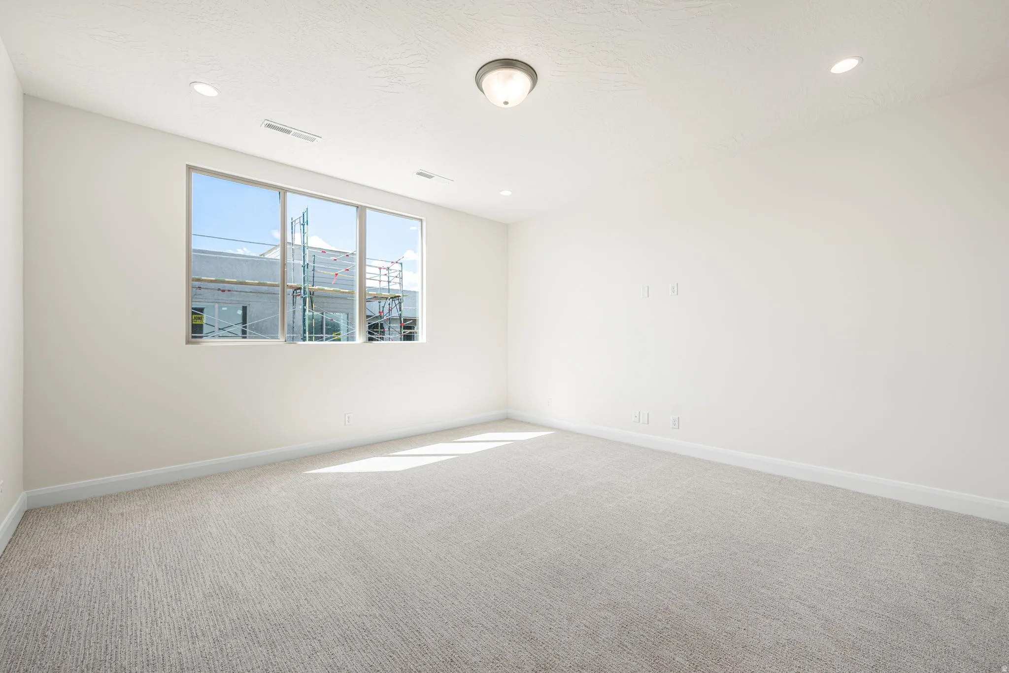Bright room featuring a three-panel window, light textured carpet, recessed lighting, and a flush-mount ceiling fixture