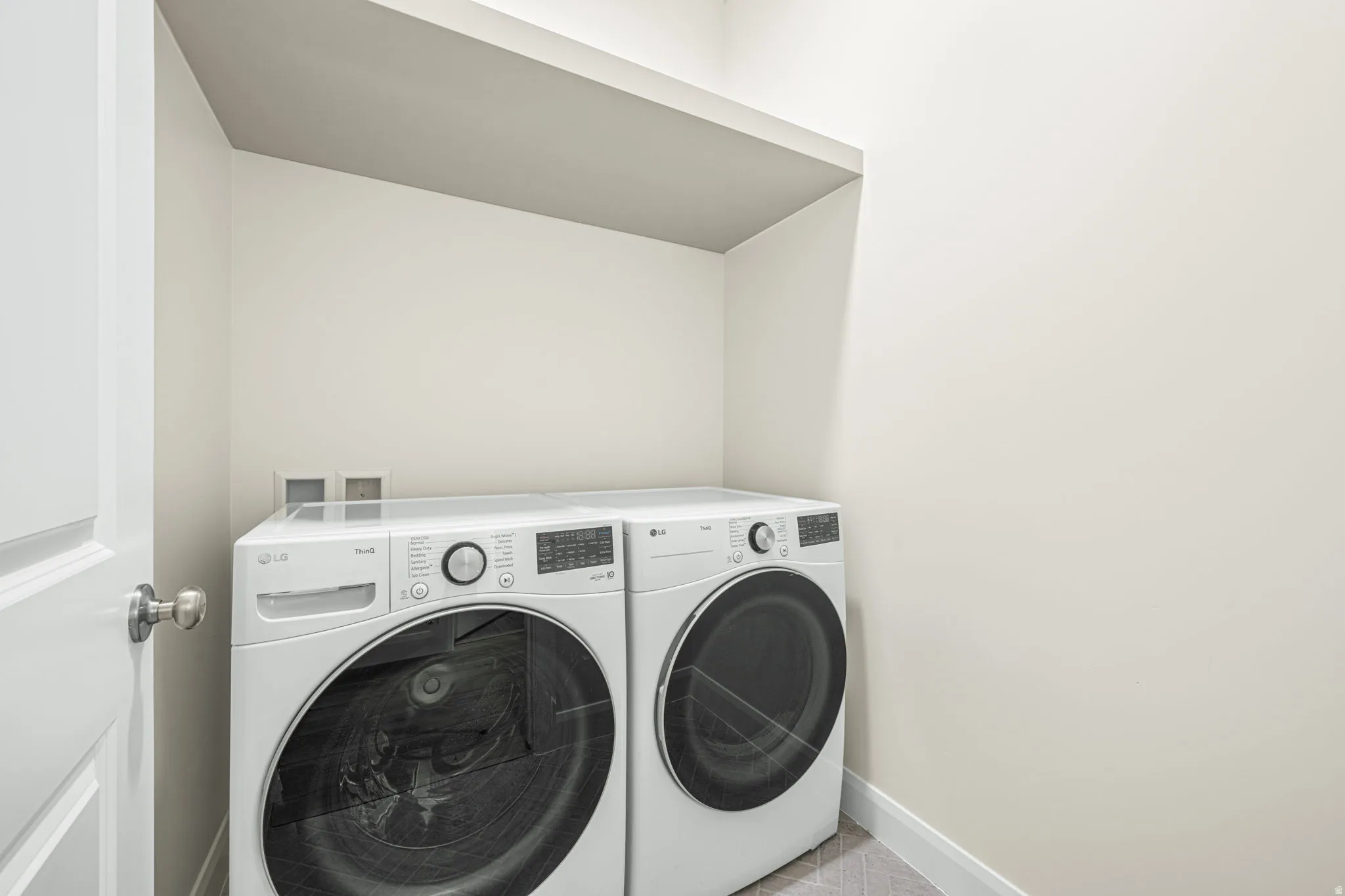 Dedicated laundry space featuring a white paneled door with brushed nickel hardware, light neutral walls, and a built-in overhead shelf