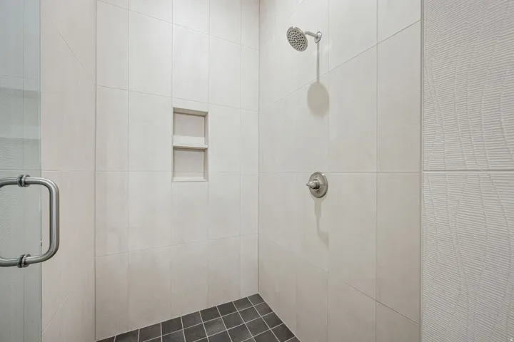 Walk-in shower with light-toned rectangular wall tiles, a built-in shower niche, a brushed nickel shower head and control, and dark square floor tiles