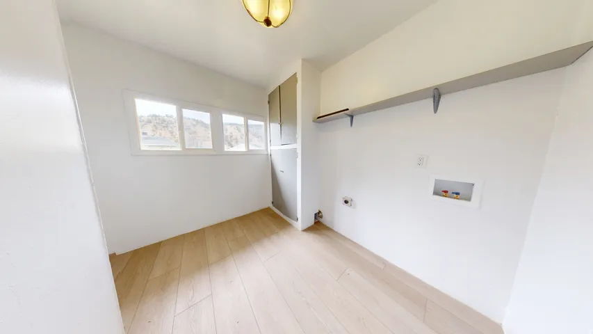 Utility room featuring wood-finish flooring, multiple windows, a built-in storage cabinet, and a wall-mounted shelving unit