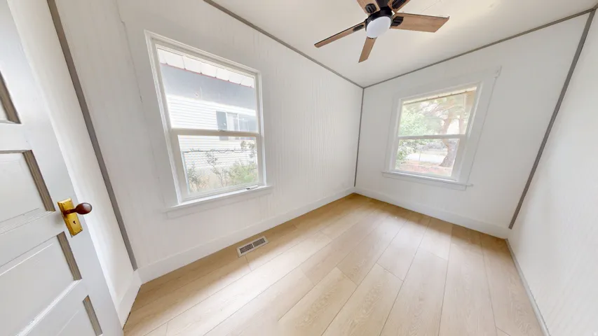Bright room featuring two single-hung windows, light wood-finish flooring, and a ceiling fan