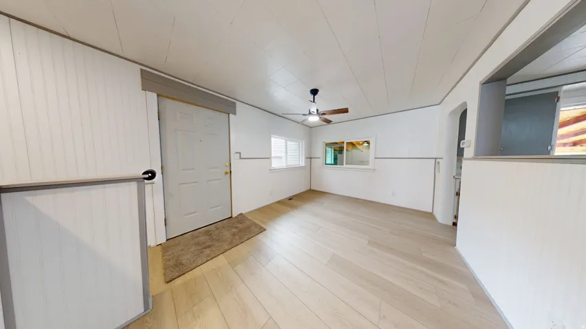 Spacious room featuring light wood-finish flooring, white paneling, and a contemporary ceiling fan with integrated lighting