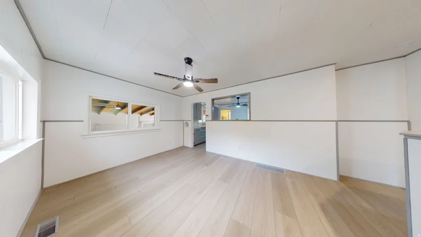 Bright room with light wood-finish flooring, white walls, and a white ceiling with a ceiling fan