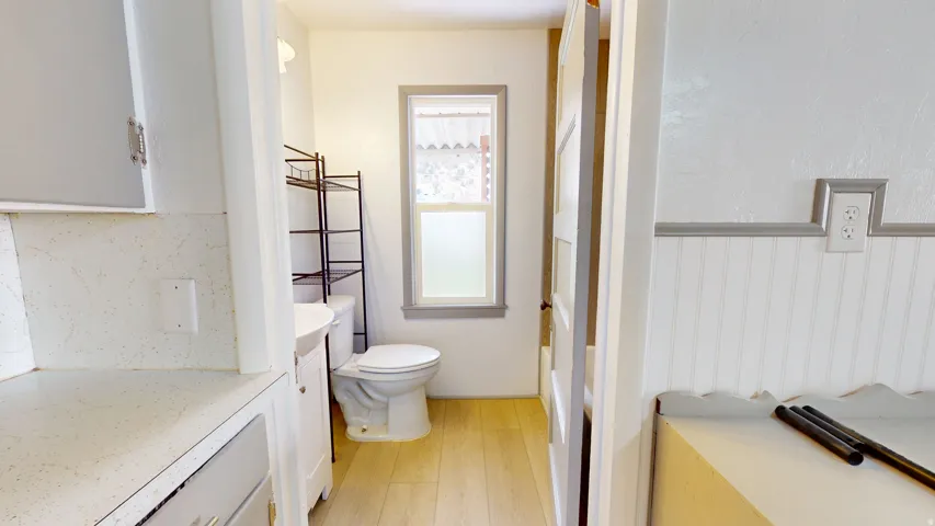 Bathroom featuring a white toilet, light-toned wood-finish flooring, and a frosted window