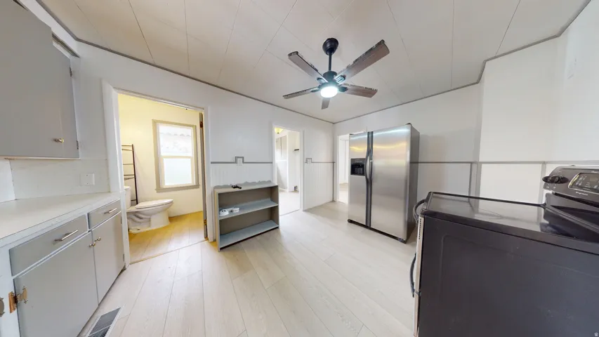Kitchen featuring light wood-finish flooring, a ceiling fan with integrated lighting, stainless steel side-by-side refrigerator, and a black range