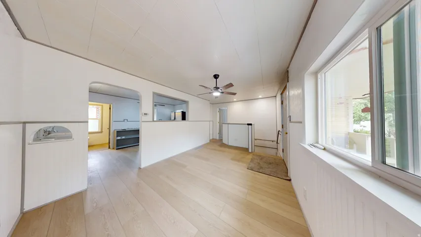 Open-concept living space featuring wood-finish flooring, a ceiling fan with integrated lighting, and a large window providing natural illumination