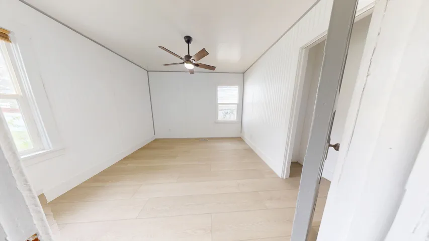 Room featuring light wood-finish flooring, white panel walls, and a ceiling fan with integrated lighting