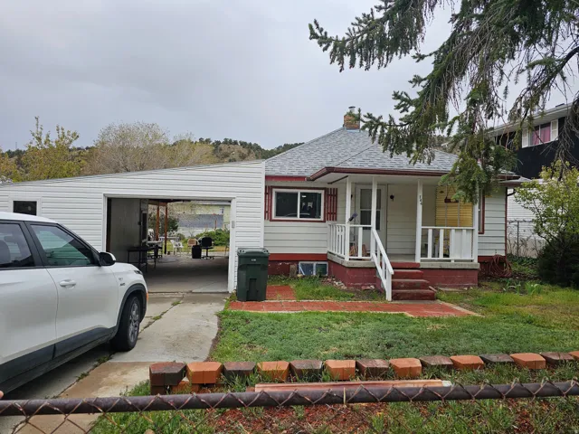 View of front of home featuring a chimney, covered porch, a shingled roof, an attached carport, and a front lawn
