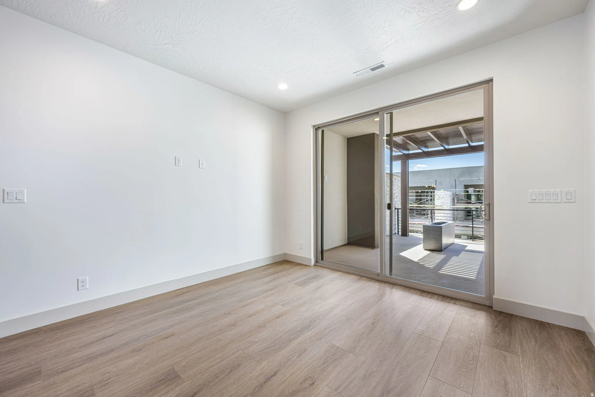 Spacious room featuring light wood-finish flooring, recessed lighting, and a glass sliding door opening to an outdoor patio with a pergola
