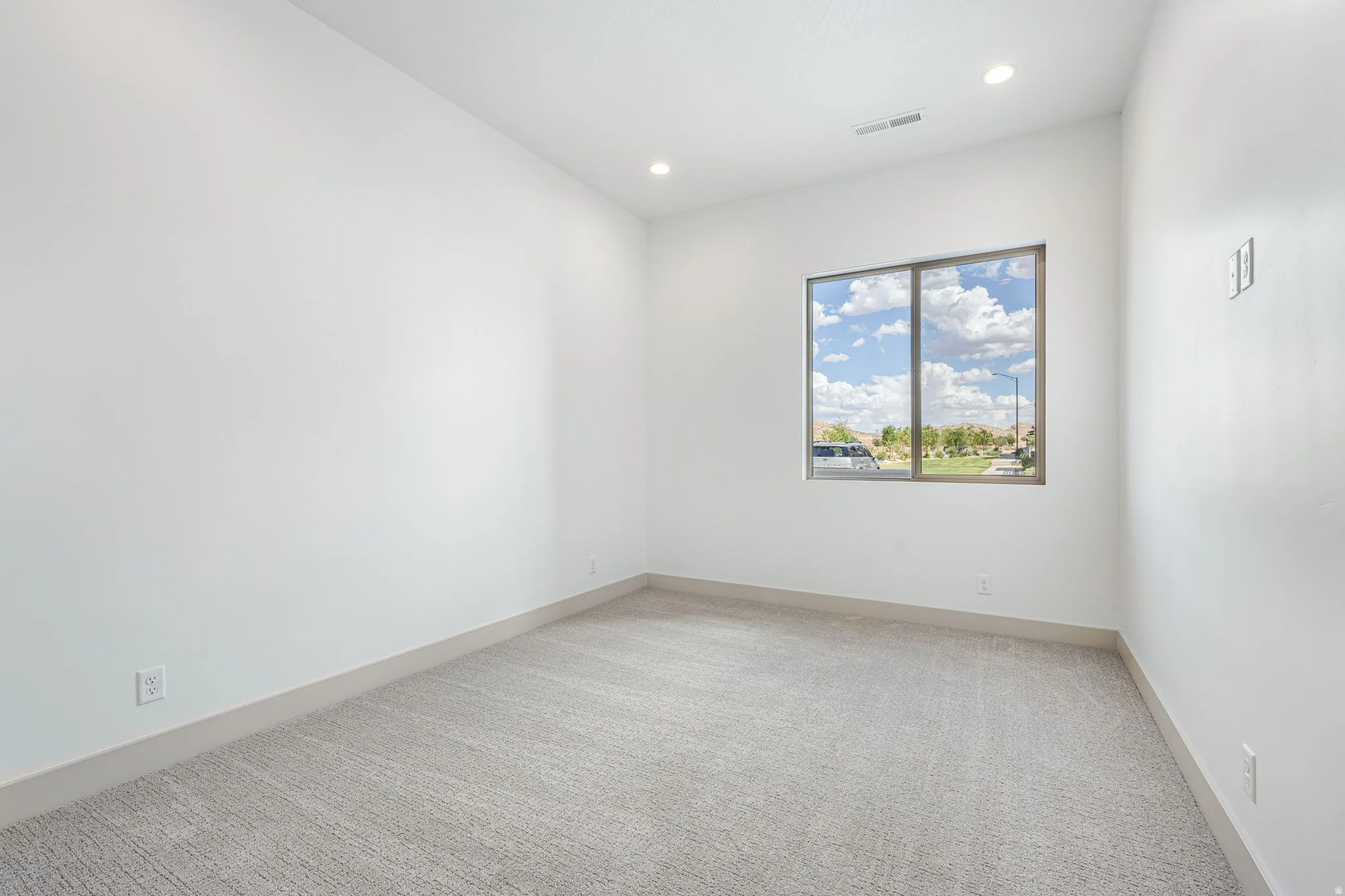 Bright interior space featuring a window with exterior scenery, overhead recessed lighting, light-colored walls, and gray patterned carpeting