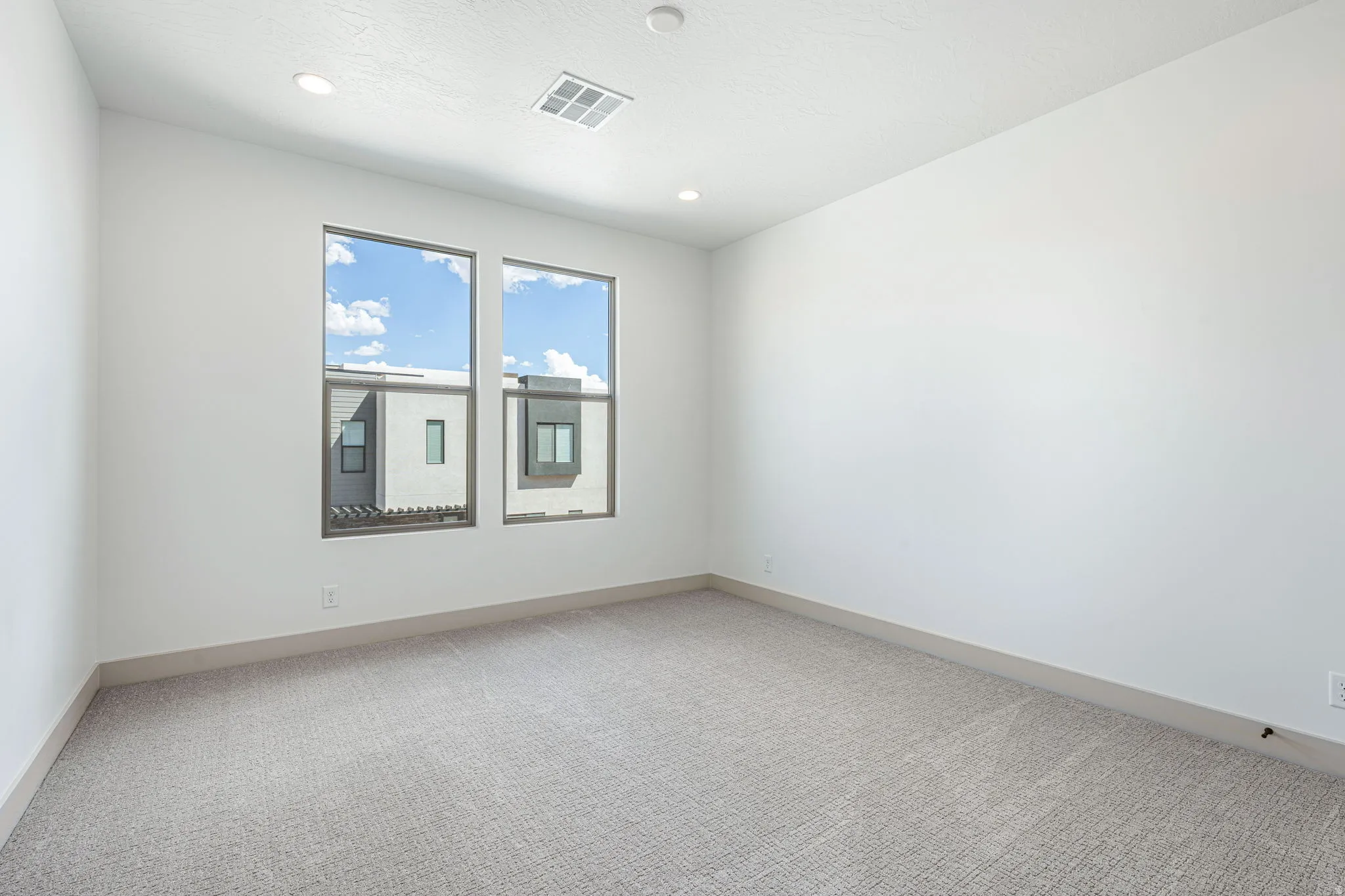 Bright room featuring two large windows, white walls, recessed lighting, neutral-toned carpet flooring, and contemporary baseboards