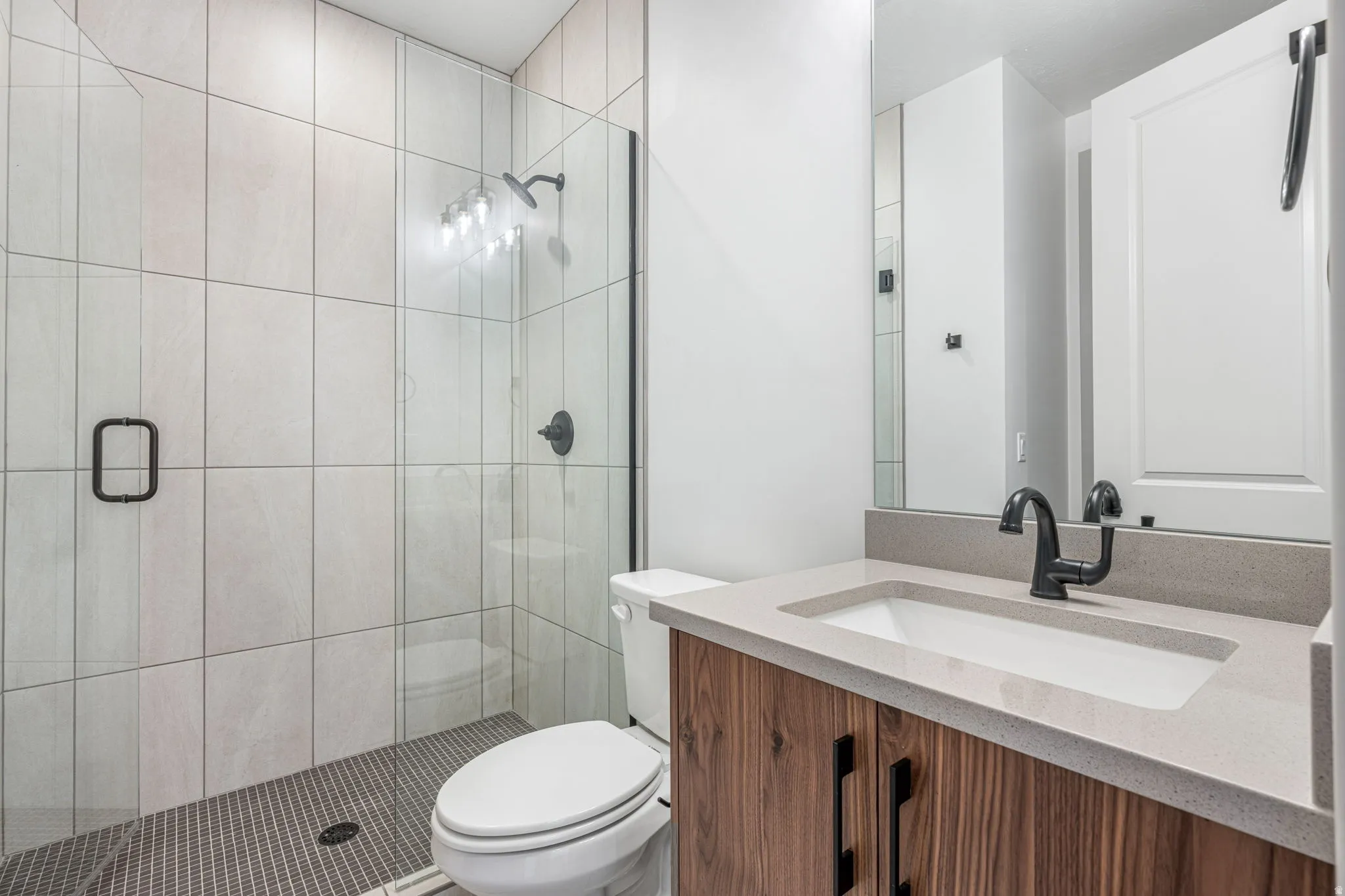 Bathroom featuring a walk-in shower with light-toned rectangular wall tiles and a dark mosaic tile floor