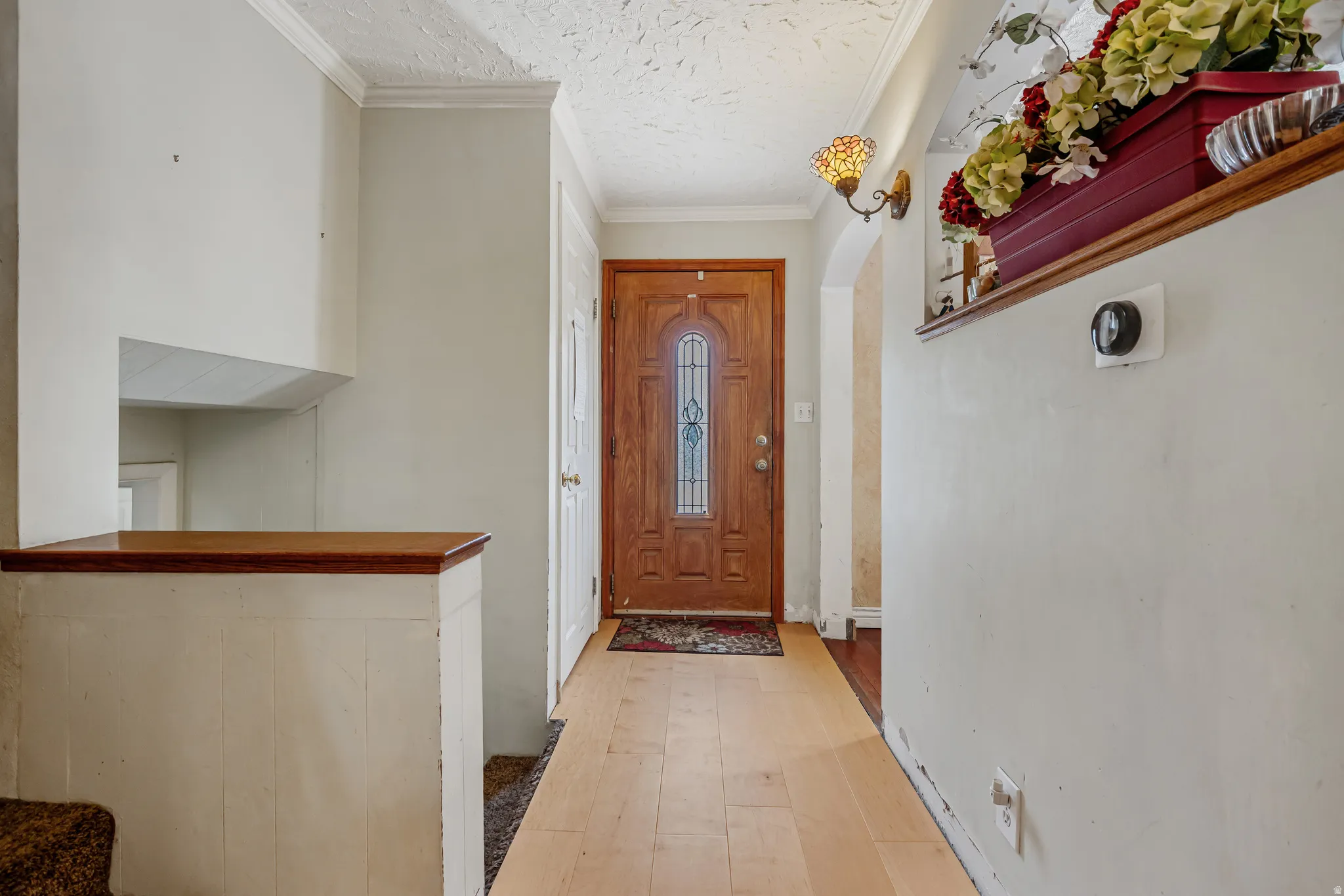 Entryway with arched walkways, crown molding, light wood finished floors, and a textured ceiling