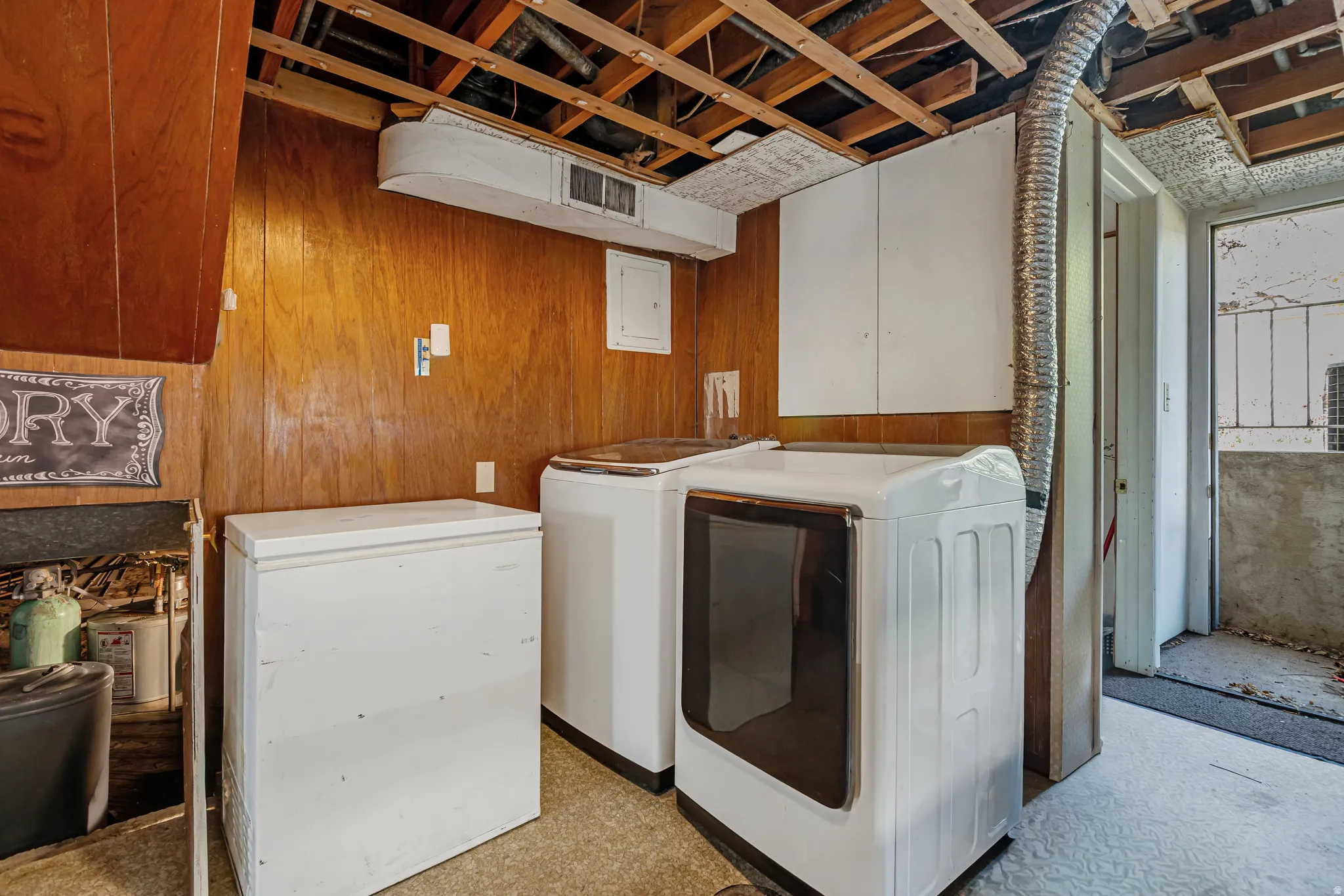 Laundry area with independent washer and dryer, light flooring, wooden walls, and electric panel