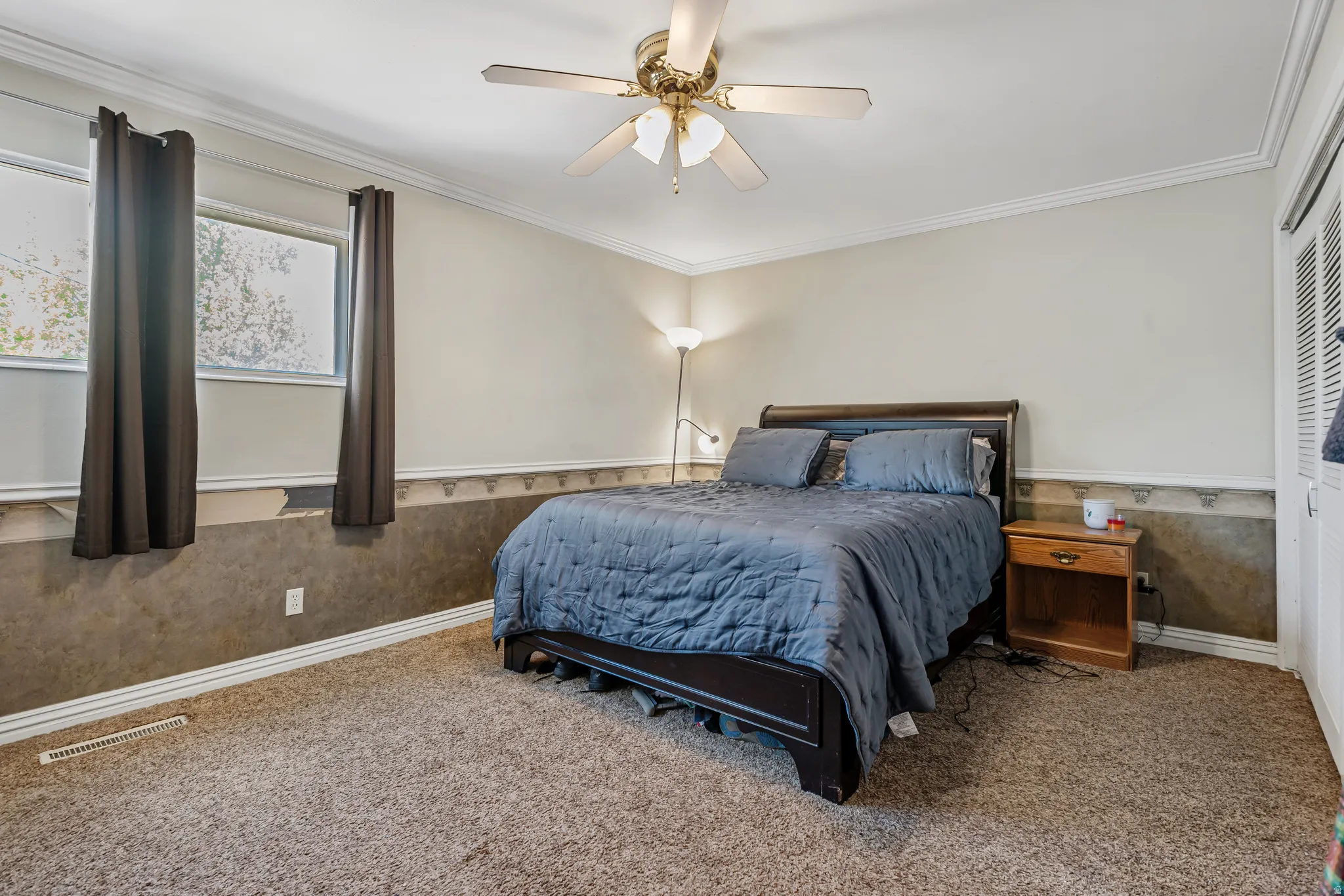 Carpeted bedroom with wainscoting, a ceiling fan, and crown molding