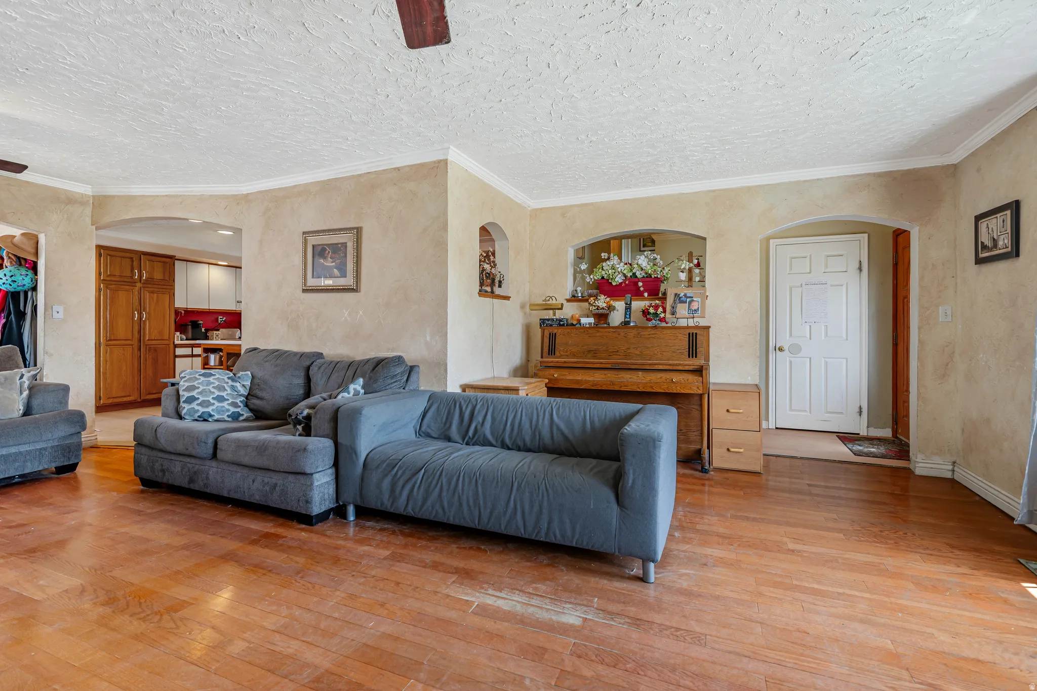 Living area featuring arched walkways, ornamental molding, ceiling fan, light wood finished floors, and a textured ceiling