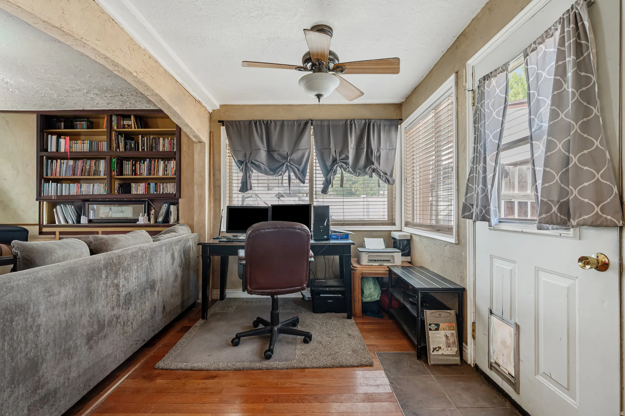 Home office with a ceiling fan, wood-type flooring, a textured ceiling, and built in shelves