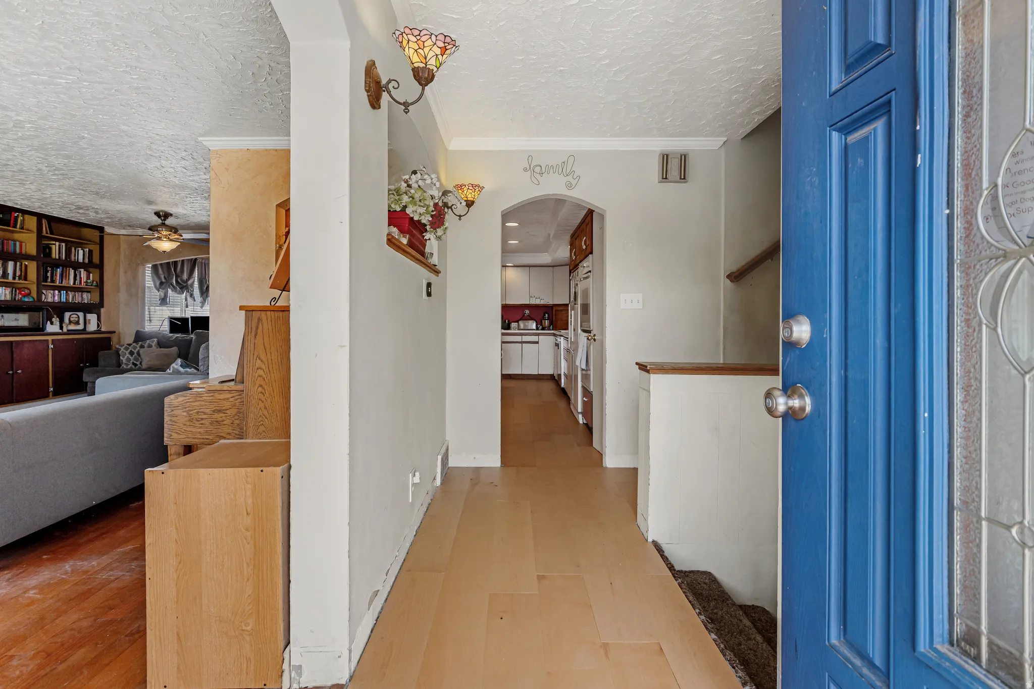 Corridor with a textured ceiling, arched walkways, light wood-style floors, and ornamental molding