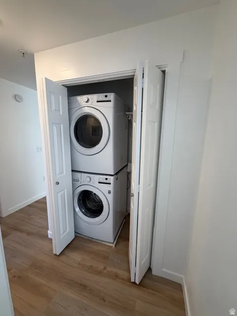 Laundry area with stacked washing machine and dryer and light wood-type flooring
