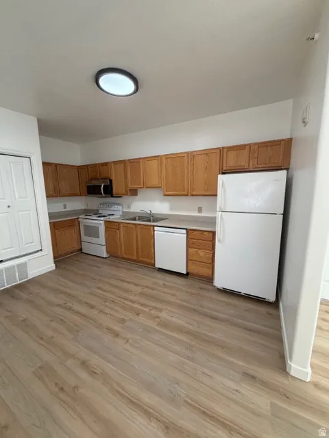 Kitchen featuring white appliances, light countertops, light wood-style flooring, and wood finish cabinets