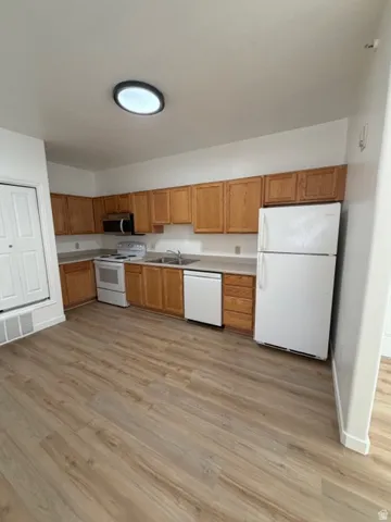 Kitchen featuring white appliances, light countertops, light wood-style flooring, and wood finish cabinets