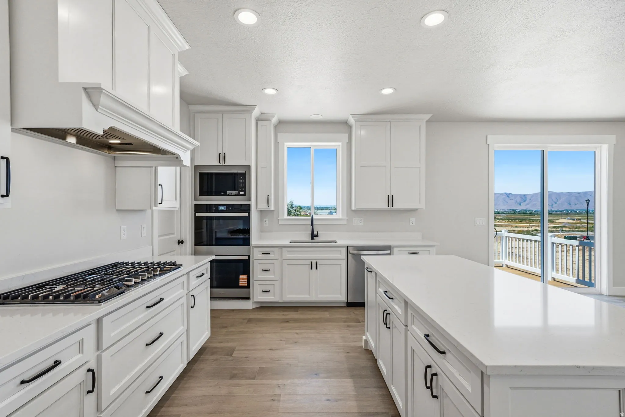 Contemporary kitchen featuring white cabinetry, a large center island with a stone countertop, stainless steel appliances including a wall oven and microwave, a gas range with an ornate range hood, and wood-finish flooring